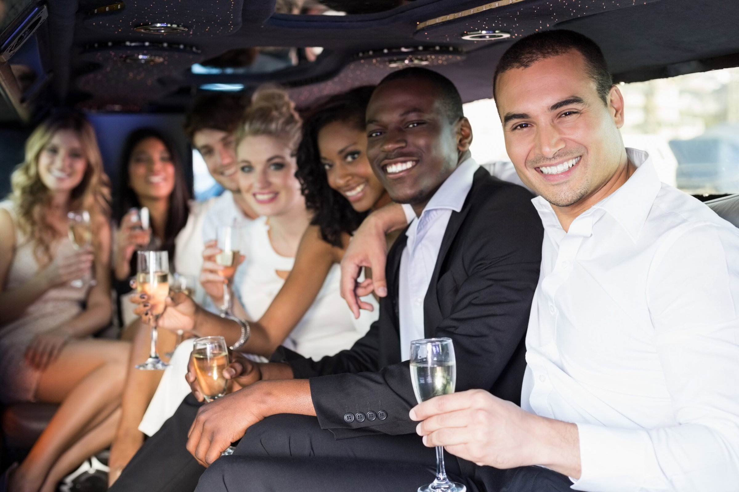 A group of people dressed formally are sitting inside a wedding limo in Austin, Texas, smiling and holding glasses of champagne.